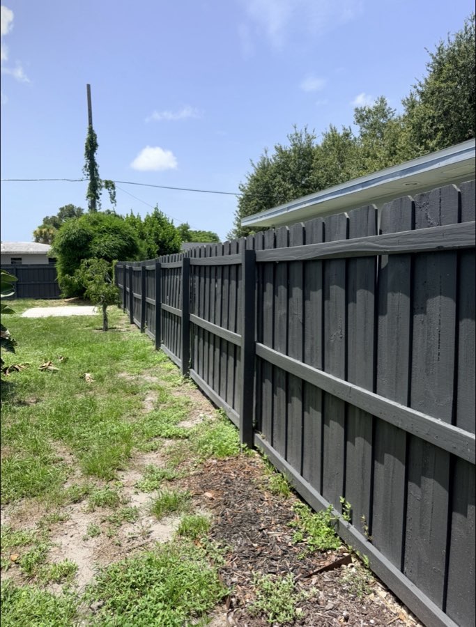 Freshly painted charcoal-black wood privacy fence along a backyard