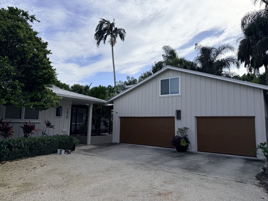 Repainted gray board-and-batten home exterior with wood-tone garage doors